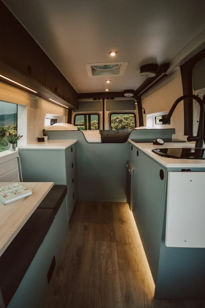 Finished campervan interior with teal cabinetry, bed and kitchen